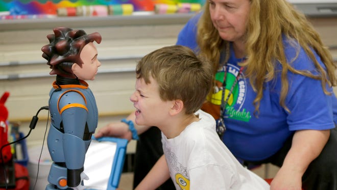 Logan Lucas, an eight-year-old 2nd grader at Shady Lane Elementary School student mimics the face made by robot Milo as Karen Richie, a Shady Lane Elementary School special education teacher observes.