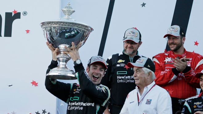 Simon Pagenaud holds up the Astor Cup after winning the 2016 IndyCar championship as team owner Roger Penske, lower right, looks on.