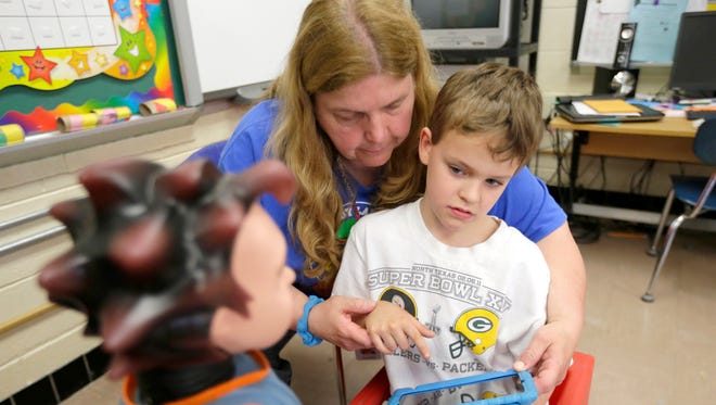 Karen Richie, a Shady Lane Elementary School special education teacher helps Logan Lucas, an eight-year-old 2nd grader at Shady Lane Elementary School student with an iPad while working with the robot Milo.