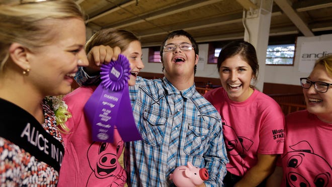 Garret Crowe, a Waukesha West High School student, smiles after he showed a pig at the Wisconsin State Fair. From left, Crystal Siemers-Peterman, the 70th Alice in Diaryland, gives him the ribbon while Isabelle Dougherty and Elysa Dougherty celebrate his success Thursday at the All for One Swine Show.