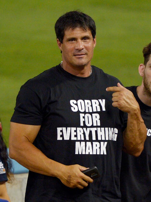 Jose Canseco points to a t-shirt that apologizes to Mark McGwire for outing him as a performance enhancing drug user during the Dodgers' game against the Cardinals in 2012 in Los Angeles.